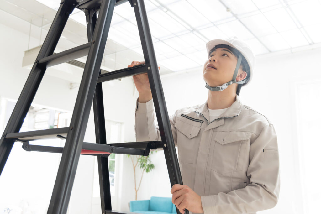 住みながらの工事。白い部屋で脚立に上がり天井まわりを施工する職人
